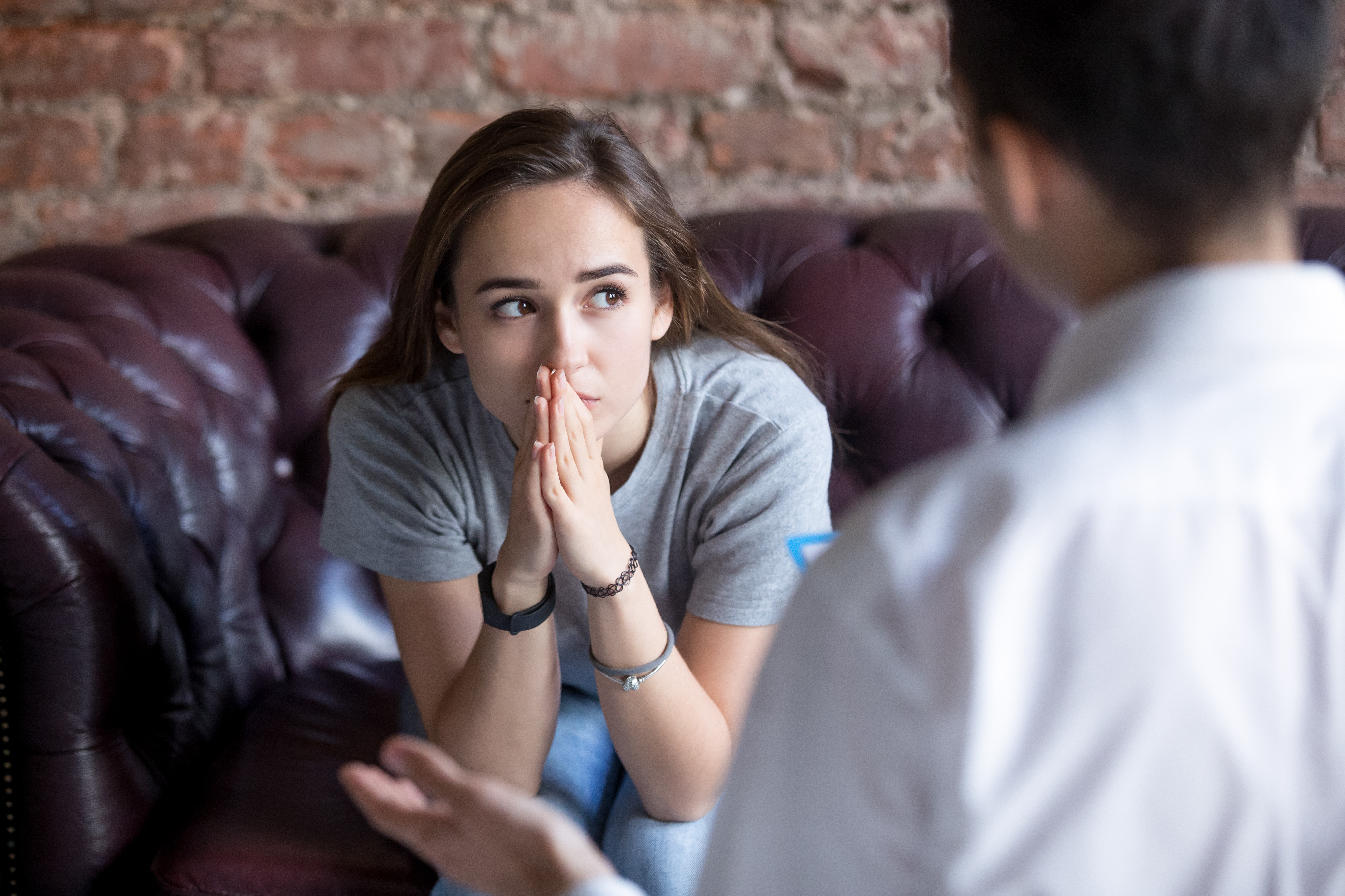 A young person listening intently with hands clasped during counseling